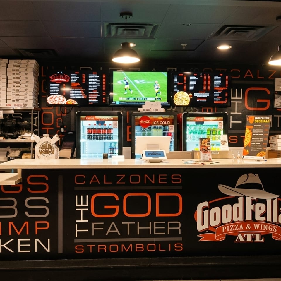 Goodfellas Pizza & Wings ATL counter with menus, drink coolers, and stacked pizza boxes.